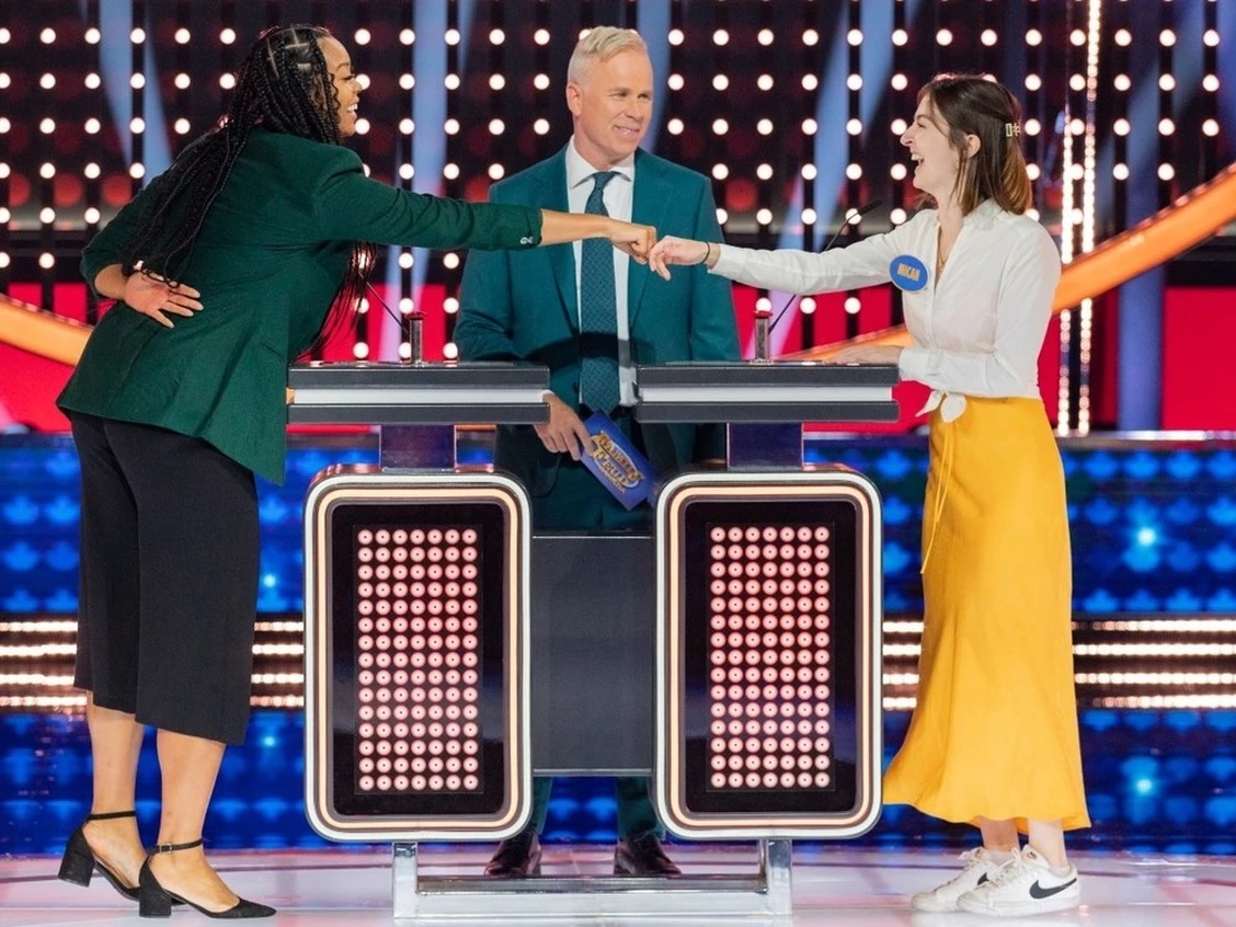 Family Feud Canada contestants fist-bumping across the podium with the host between them