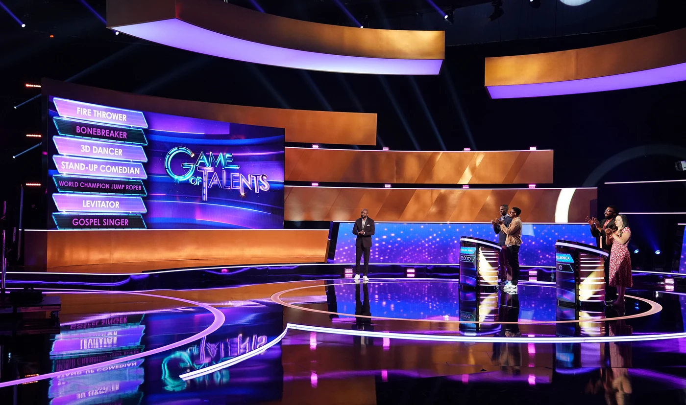 Game of Talents production set with host, contestants, podiums, and talent board